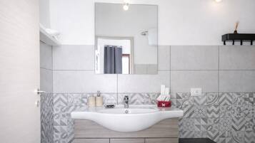 A bathroom with a white sink, a mirror above it, patterned tiles, a small stool, and a shelf with a candle.