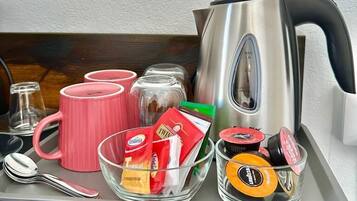 A tray with a kettle, pink mugs, a glass bowl with snacks, and a spoon.