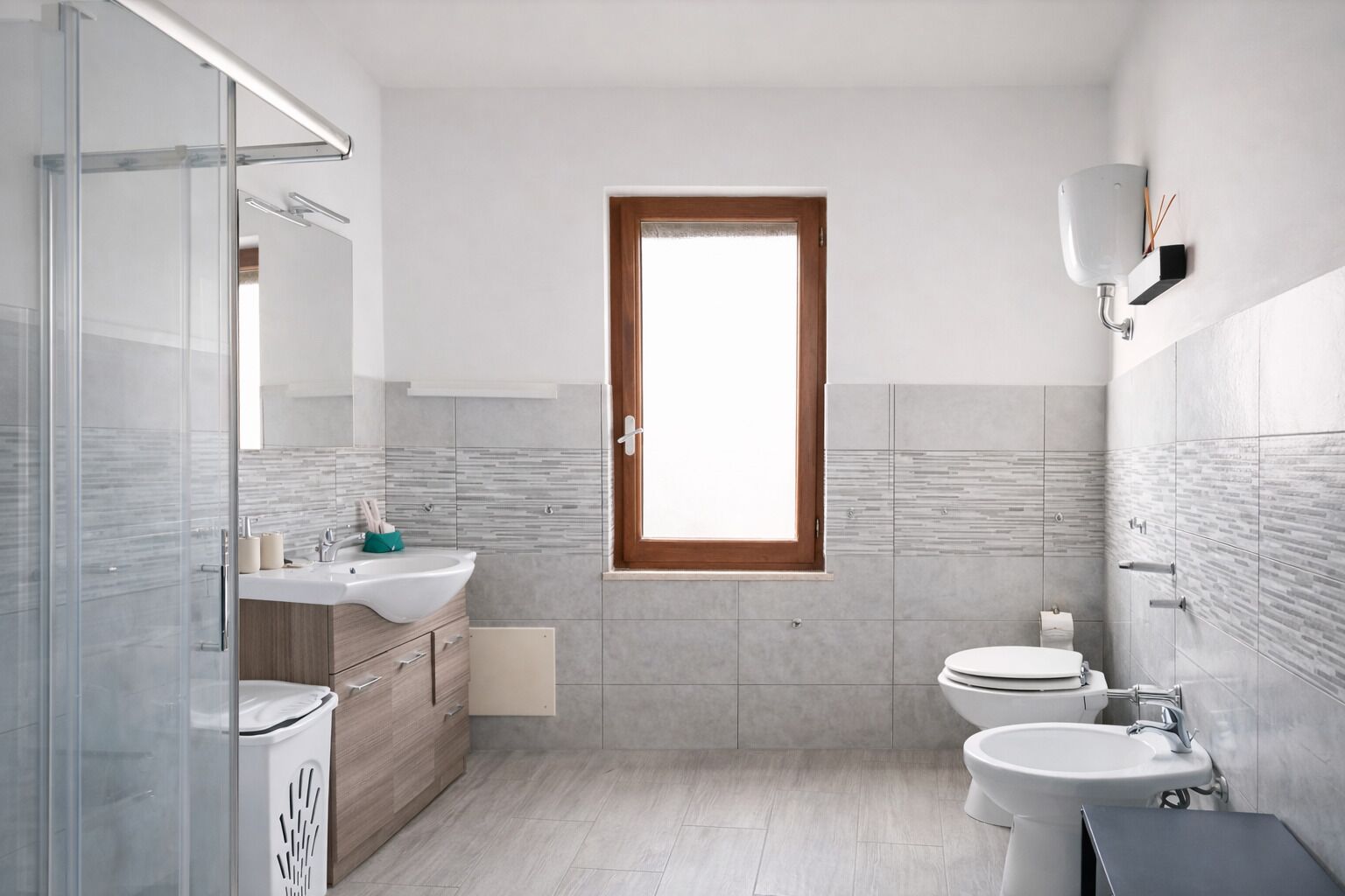 Un baño moderno con cabina de ducha de vidrio, tocador de madera, inodoro y lavamanos.