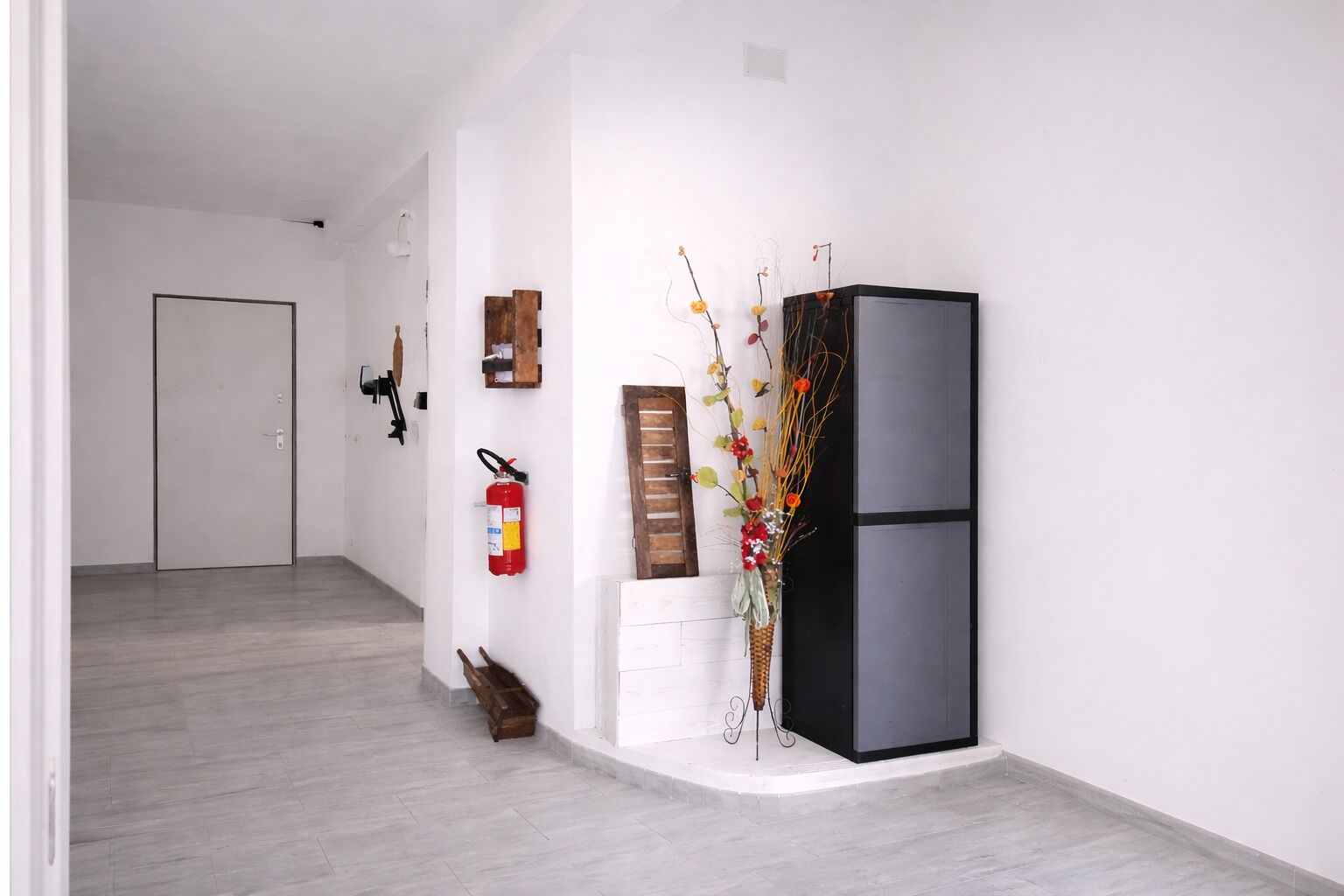 A hallway with a wooden bench, a fire extinguisher, a black refrigerator, and a wall-mounted wooden shelf.