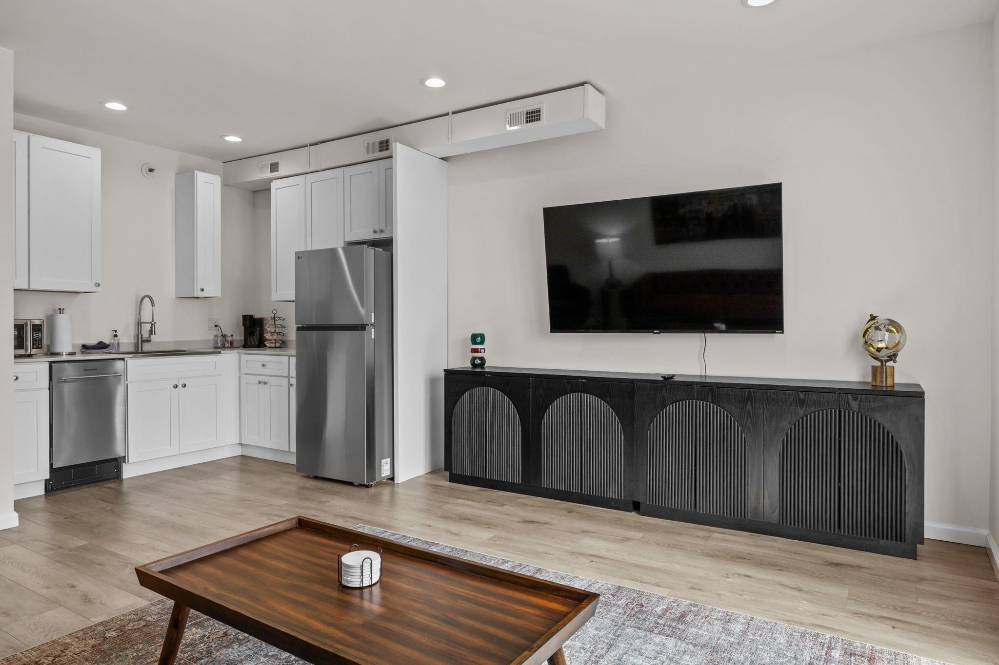A modern kitchen with white cabinetry, a stainless steel refrigerator, and a flat-screen TV mounted on the wall.
