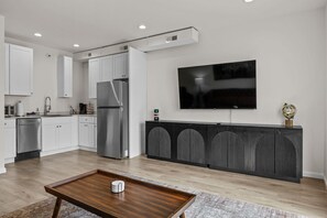 Una cucina moderna con mobili bianchi, un frigorifero in acciaio inossidabile e una TV a schermo piatto montata a parete.