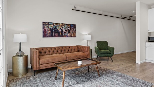 Una sala de estar con un sofá marrón, un sillón verde, una mesa de centro y un cuadro en la pared.