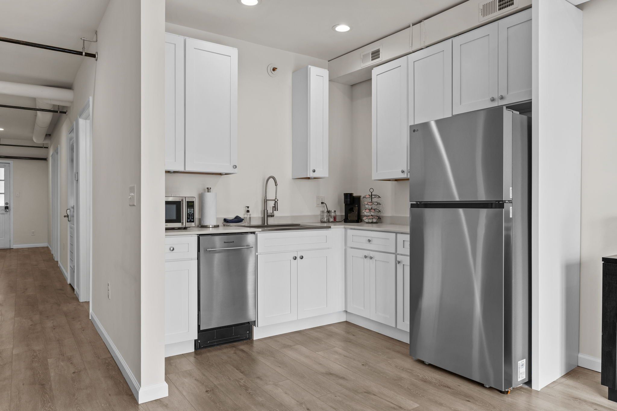 A modern kitchen with white cabinetry, stainless steel appliances, and a wooden floor.