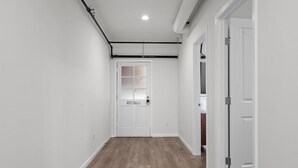 Un pasillo con suelo de madera, paredes blancas y una puerta con ventanal.