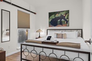 Un dormitorio moderno con cama, mesita de noche, lámpara y una obra de arte.