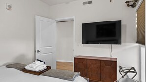 Un dormitorio con una cama, un televisor en la pared, un armario de madera y una silla.