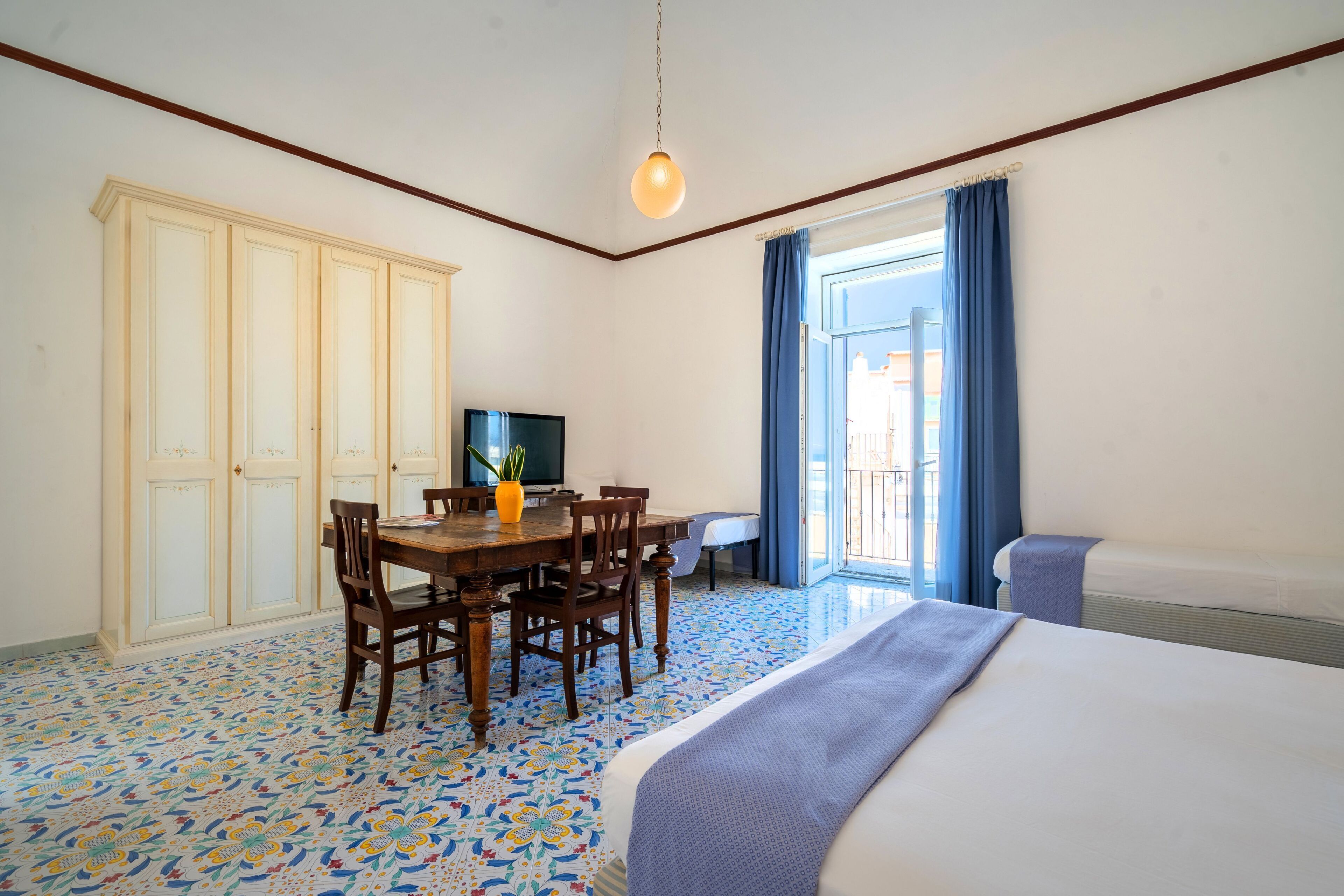 Una habitación con cama, una mesa de comedor con sillas, televisor y una ventana con cortinas.