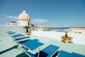 A rooftop terrace with blue lounge chairs, a white dome structure, and a view of the sea and town. - Pensione Di Lustro (Forio)
