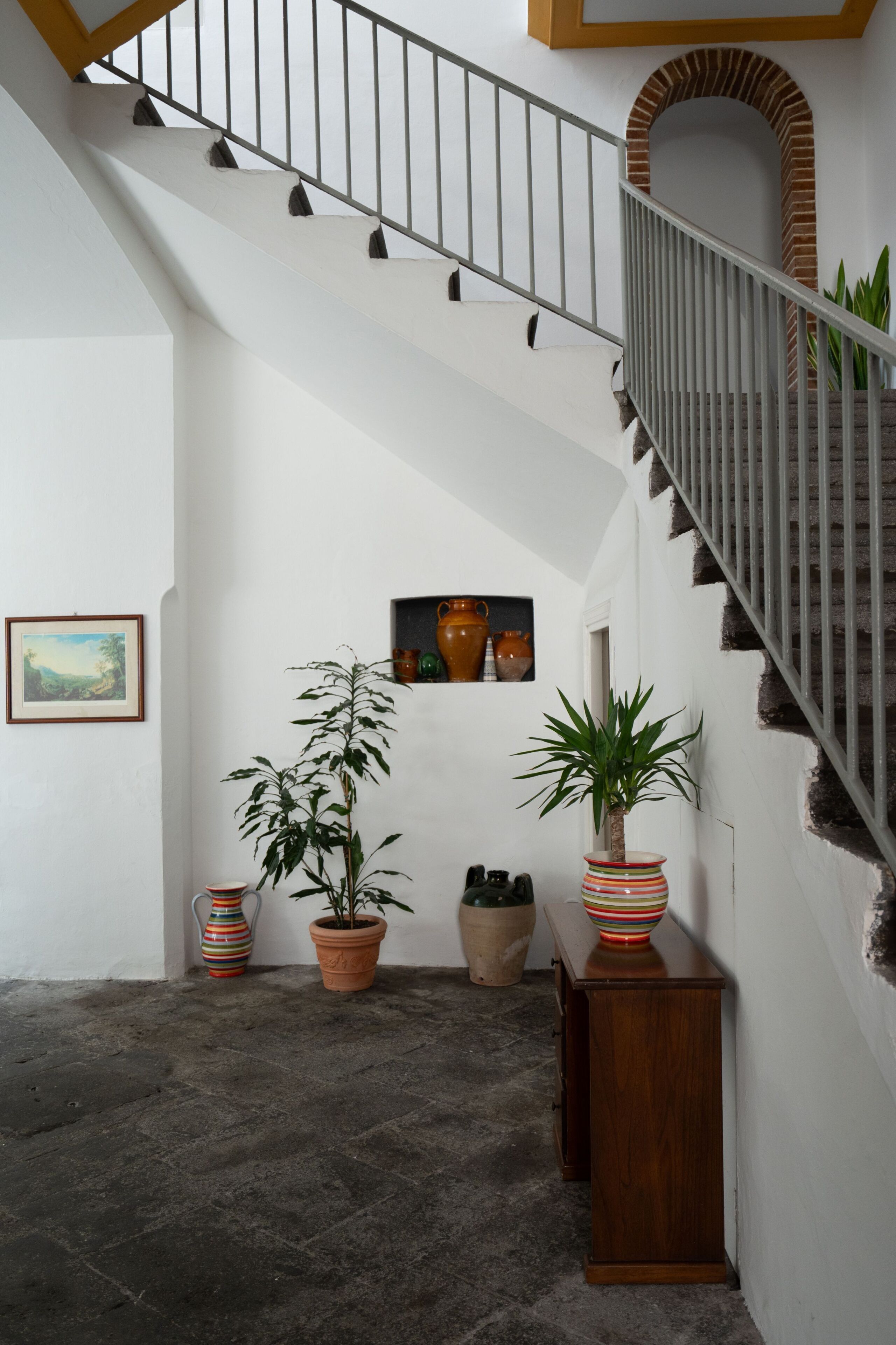 A staircase with a metal railing, a potted plant, and a wooden cabinet.