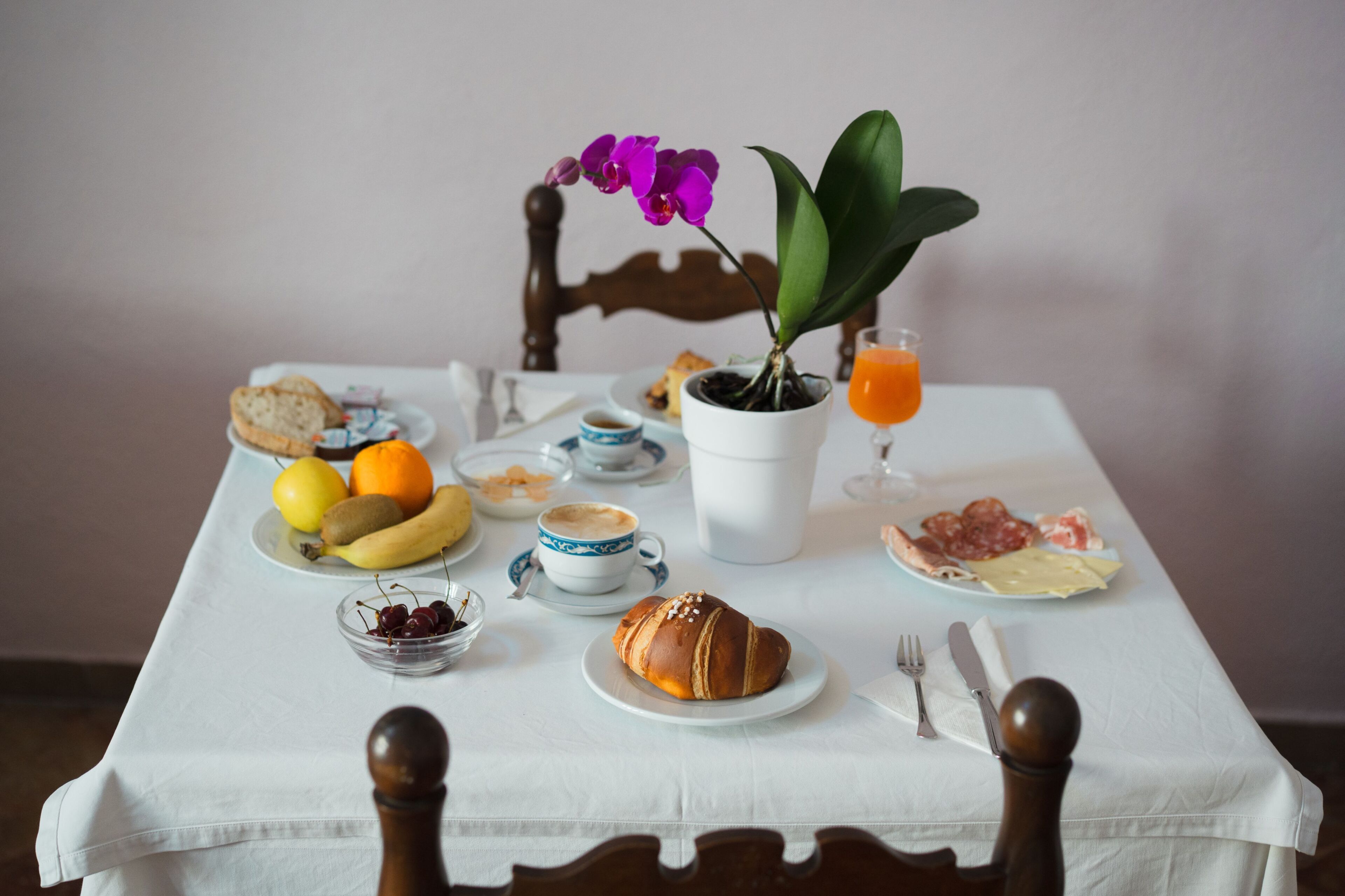 Uma mesa de café da manhã com diversos alimentos, uma planta em vaso e uma xícara de café.