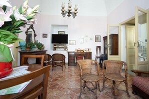 Ein Wohnzimmer mit Fernseher, Korbstühlen, einem Esstisch und einer roten Vase.