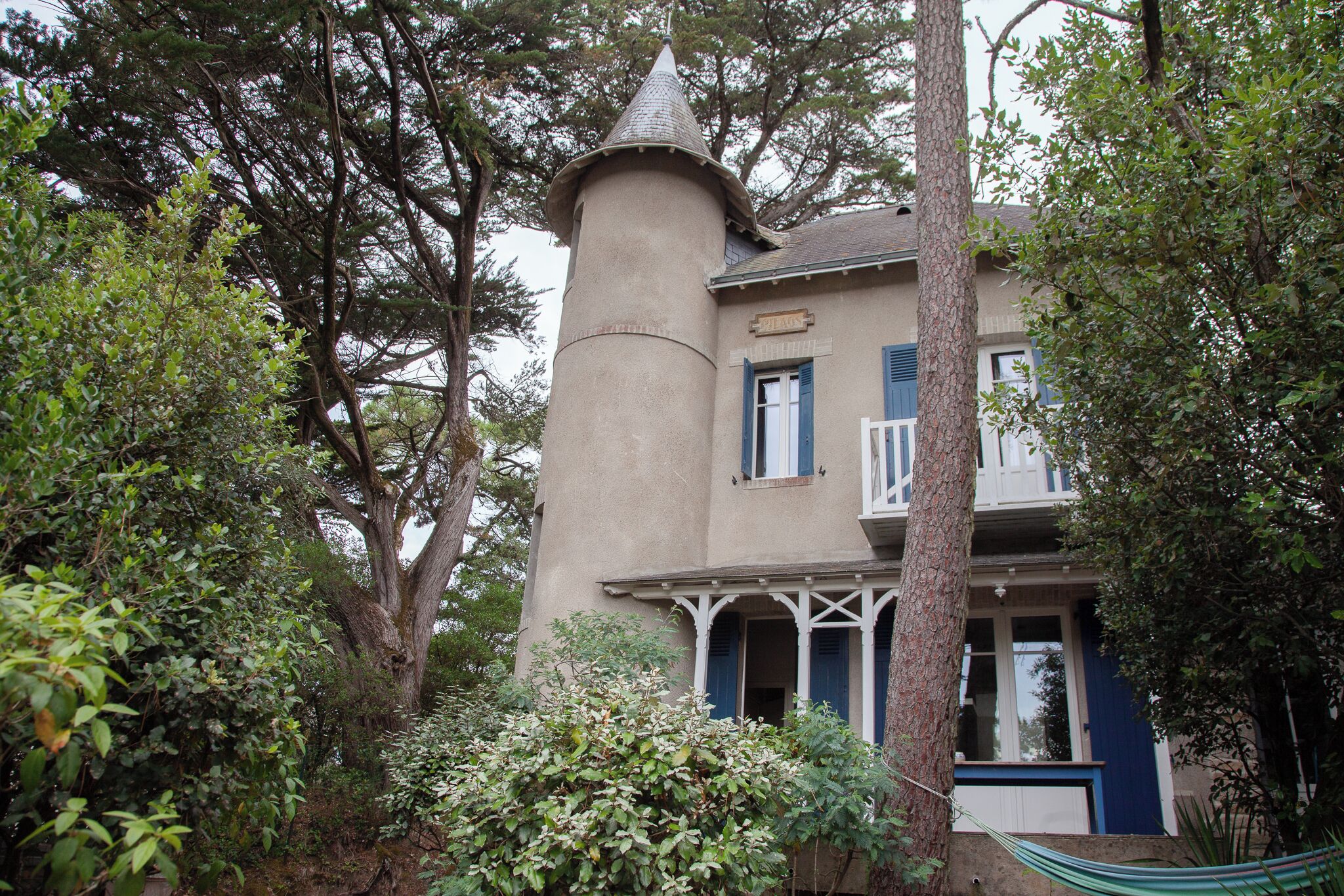 A two-story building with a tower-like structure, surrounded by trees and greenery.