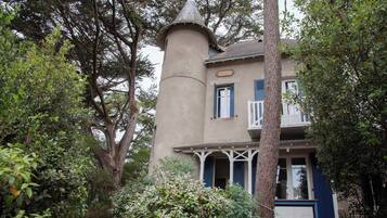 A two-story building with a tower-like structure, surrounded by trees and greenery.