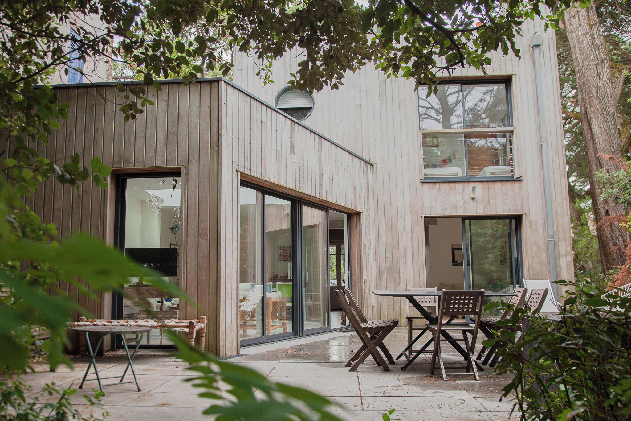 A modern building with a wooden exterior, large glass windows, and a patio area with outdoor furniture.