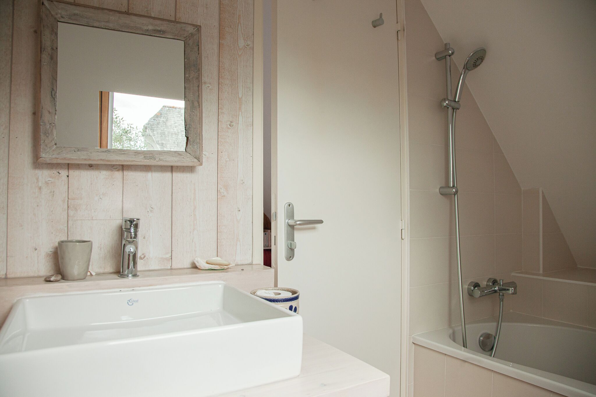 A bathroom with a white sink, a mirror, a shower, and a door.