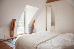 A bedroom with a sloped ceiling, a bed with white bedding, a wooden chair, and a view through a window. - Villa Pornichetaine - Beach, train station, and town center within walking distance - Sleeps 7 (Pornichet)