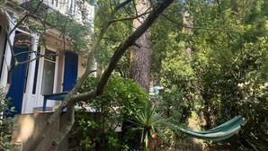 A hammock in a lush garden area with a building in the background.
