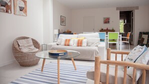 A modern living room with a sofa, wicker chair, glass coffee table, and a dining area with chairs. - Villa pornichetaine - Beach, station & center on foot- 7 people (Pornichet)
