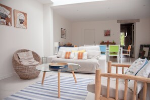 Ein modernes Wohnzimmer mit einer Couch, einem Korbstuhl, einem Glastisch und einem Essbereich mit Stühlen.
