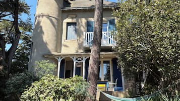 A two-story house with a porch, a large tree in front, and a hammock.