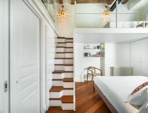 Ein Schlafzimmer mit einem Bett, einem Sessel, einer Treppe und einem Regal mit Gegenständen.