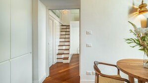 Ein Korridor mit Holzboden, einer Treppe, einem Essbereich mit rundem Tisch und Stühlen sowie einer Wandleuchte.