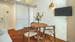 Ein Essbereich mit einem runden Holztisch, zwei Stühlen, einer Blumenvase, einem an der Wand befestigten Fernseher und einer Holzbalkendecke.