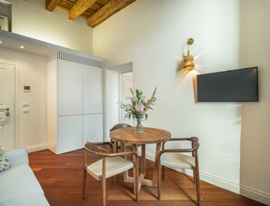 A dining area with a round wooden table, two chairs, a vase with flowers, a wall-mounted TV, and a wooden ceiling. - Rafts Bright Loft R&R (Venecia)