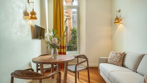 Ein Zimmer mit einem runden Holztisch, zwei Stühlen, einem Sofa und einem Fenster mit Vorhängen.