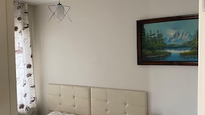 A bedroom with a bed, a ceiling fan, a painting, and a small wooden side table. - kasapoglu ceren pansiyon  (Bursa)