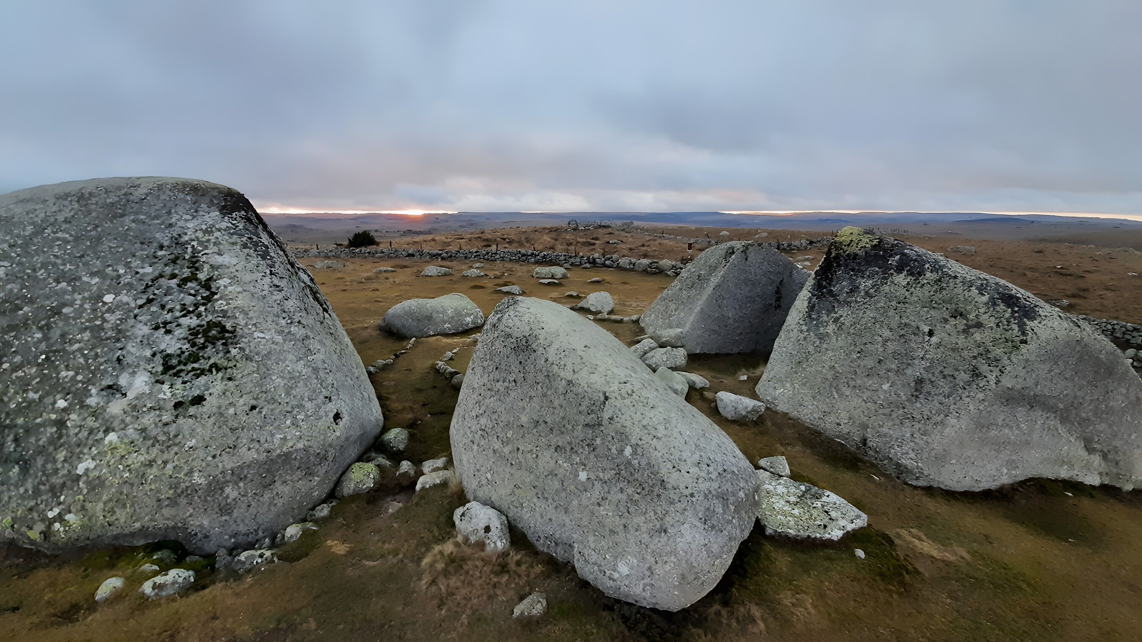 Eine felsige Landschaft mit großen Felsen und einem weiten Blick auf einen Sonnenuntergang.