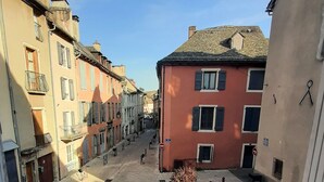 Une rue pavée, bordée de bâtiments des deux côtés, avec un banc et un bac à fleurs contenant un arbre.