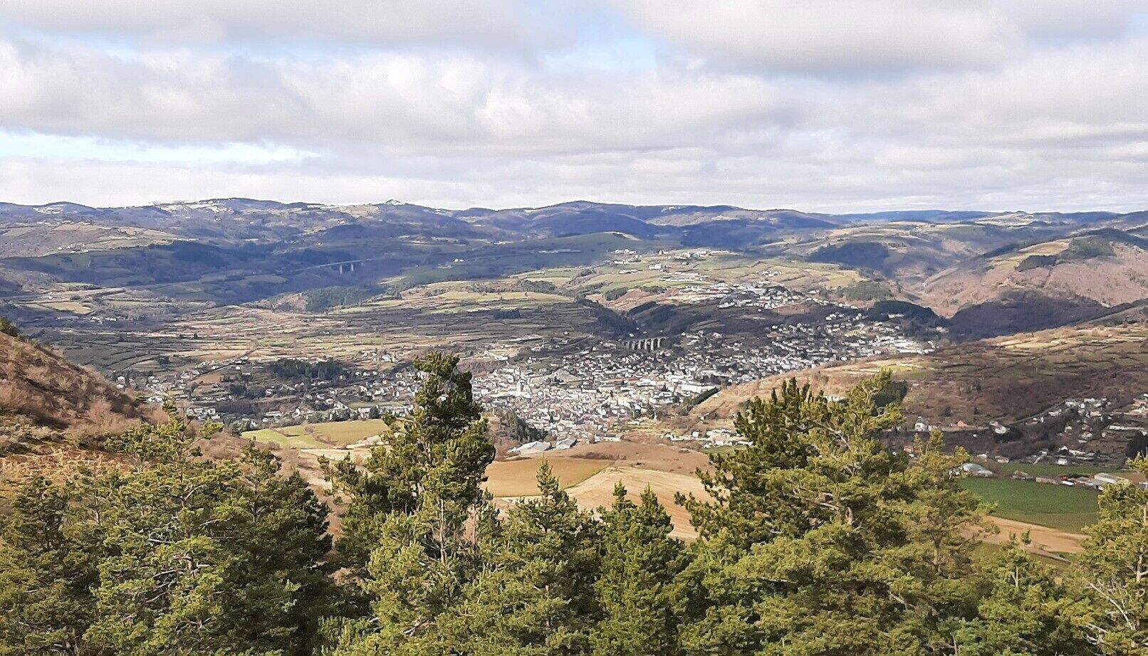 Et panoramaudsigt over en dal med en by, bløde bakker og en bro.