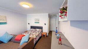 Une chambre à coucher comprenant un lit, des tables de chevet, une commode, une étagère murale agrémentée d’objets décoratifs et une porte donnant sur une autre pièce.