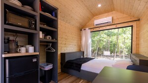 A compact room with a bed, a small table, a kitchenette, and a window with a view of trees. - Glamping at Four Fillies Lodge-The Friar Tuck (Peterstown)