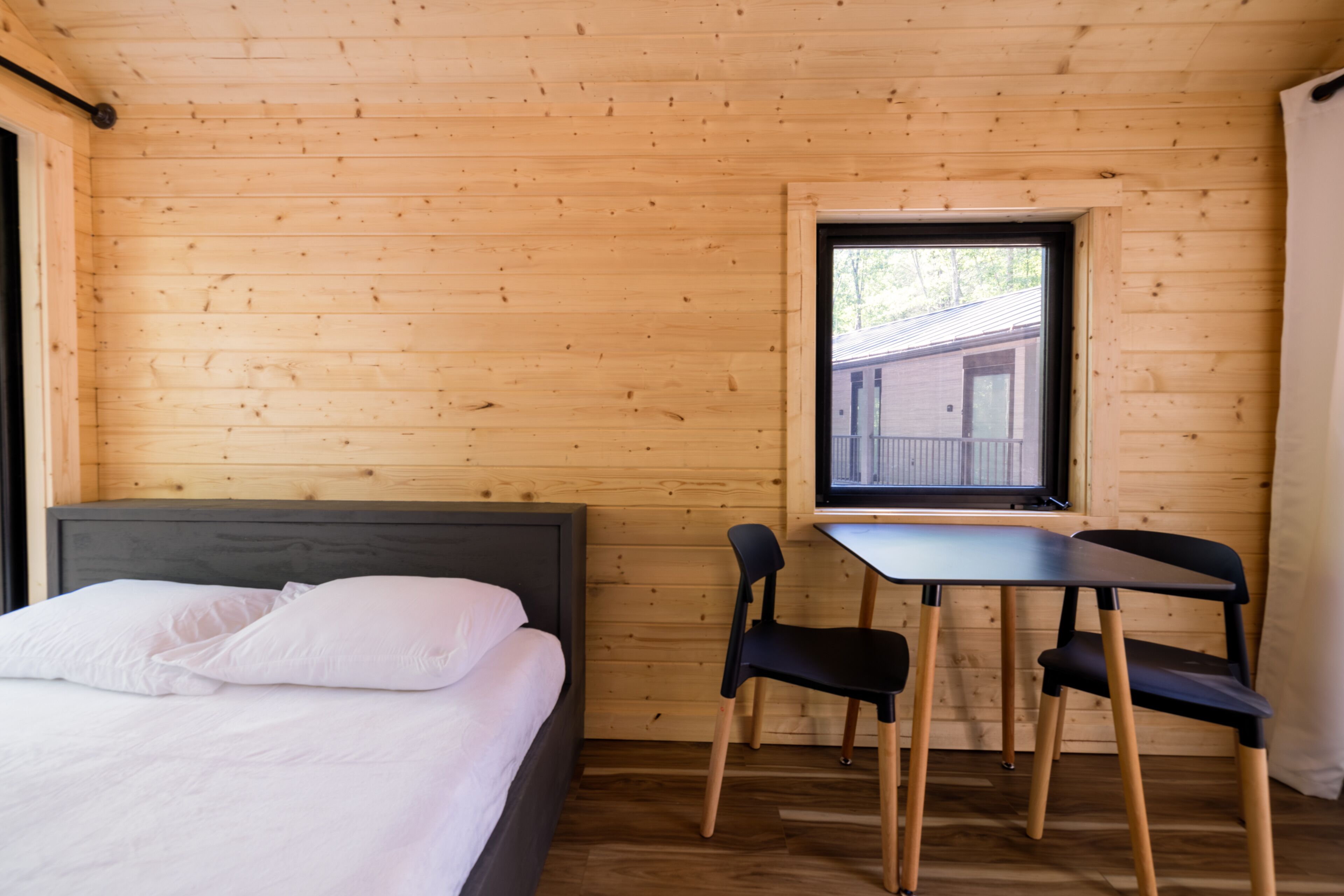 Une pièce de cabane en bois comprenant un lit, une table, deux chaises et une fenêtre.