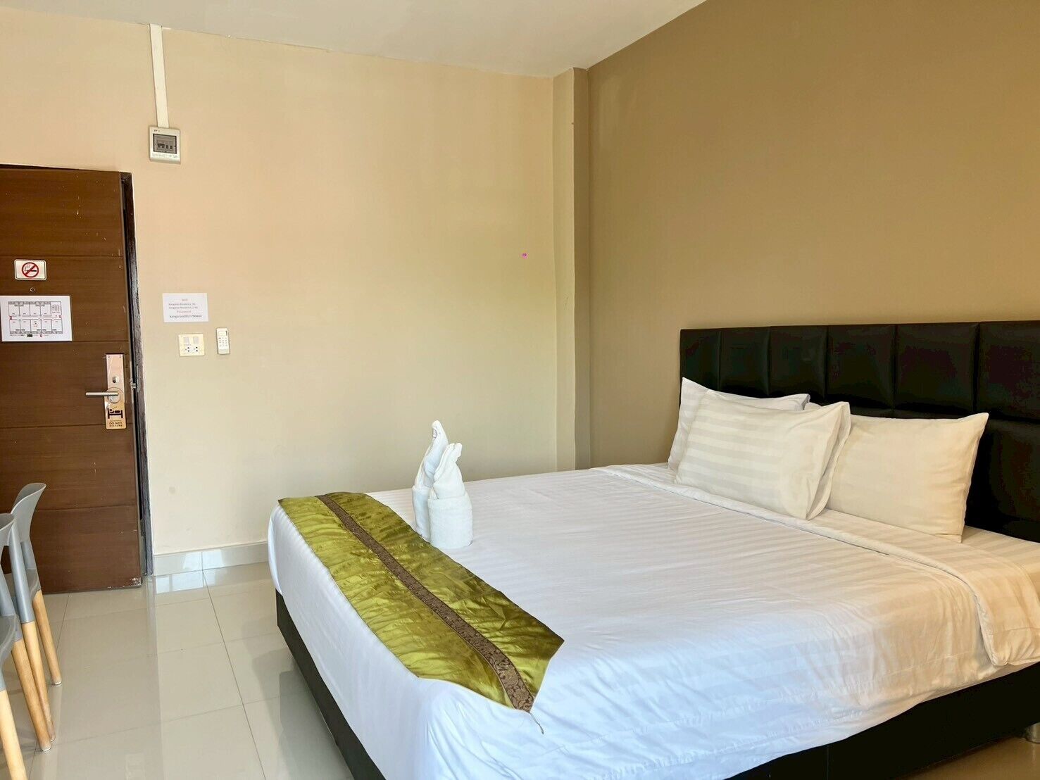 A hotel room with a bed, a chair, a door, and a wall-mounted thermostat.