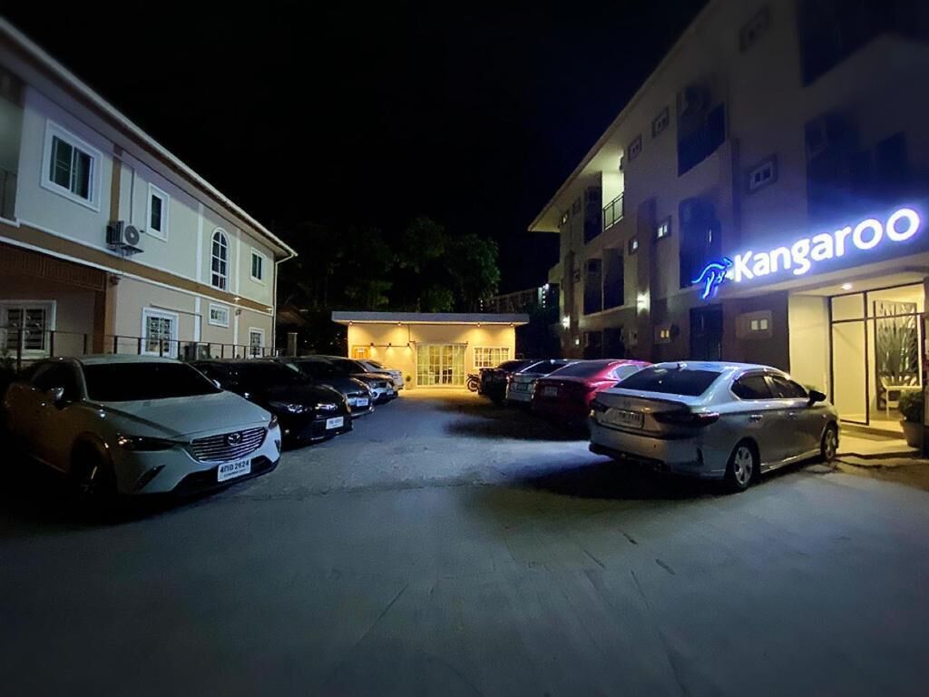 Ein Parkplatz mit mehreren Autos, ein Gebäude mit leuchtendem Neon-Schild mit dem Schriftzug 'Kangaroo' und einem gut beleuchteten Eingang.