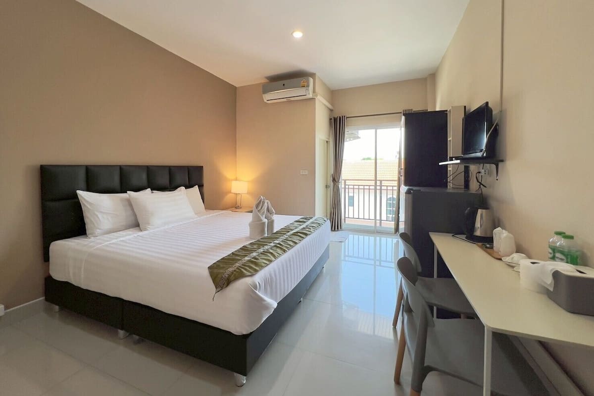 A hotel room with a bed, a desk, a chair, a TV, and an air conditioning unit.