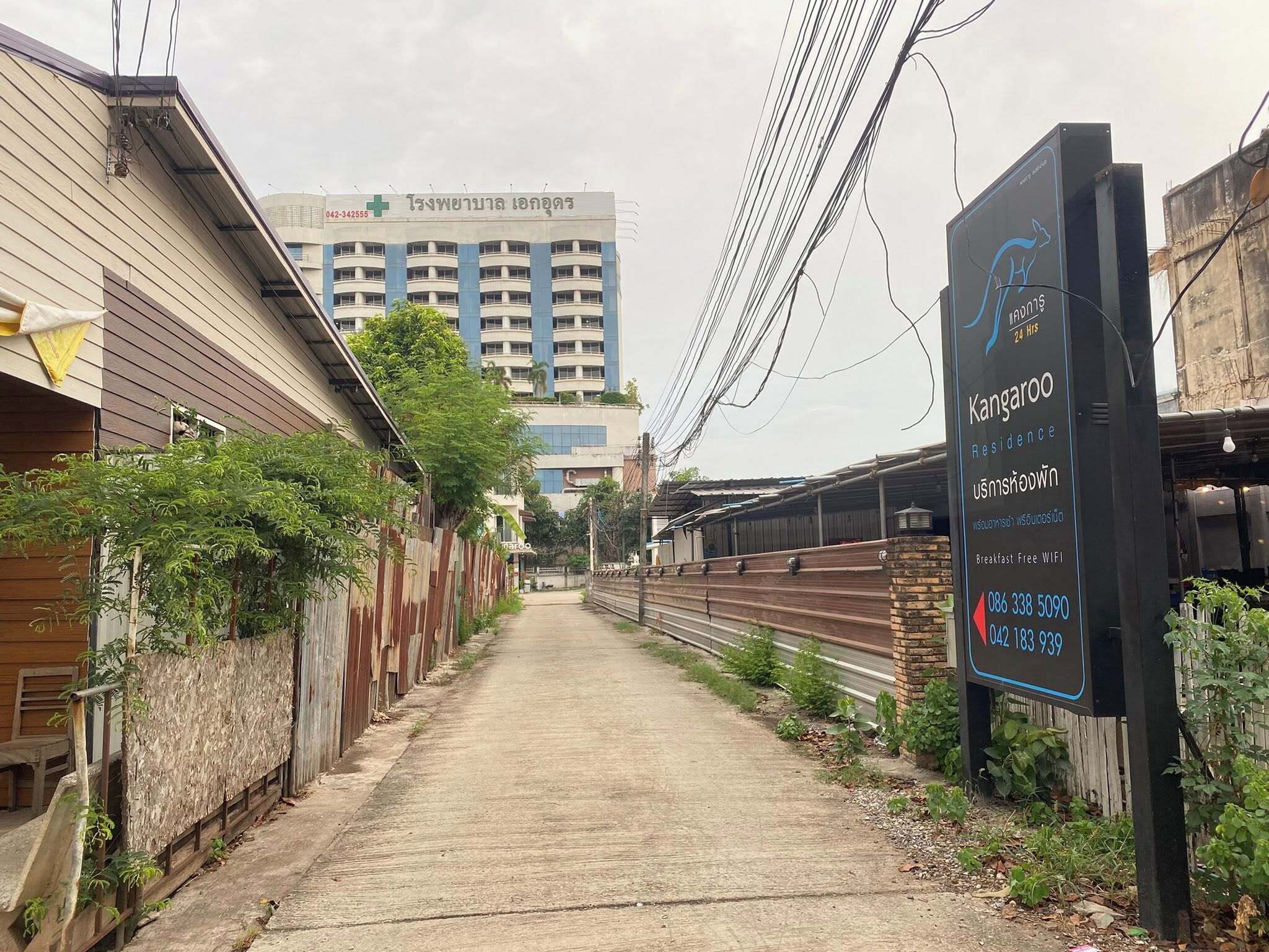A narrow alleyway with a sign for Kangaroo Residence, a building with a medical facility in the background, and overhead power lines.