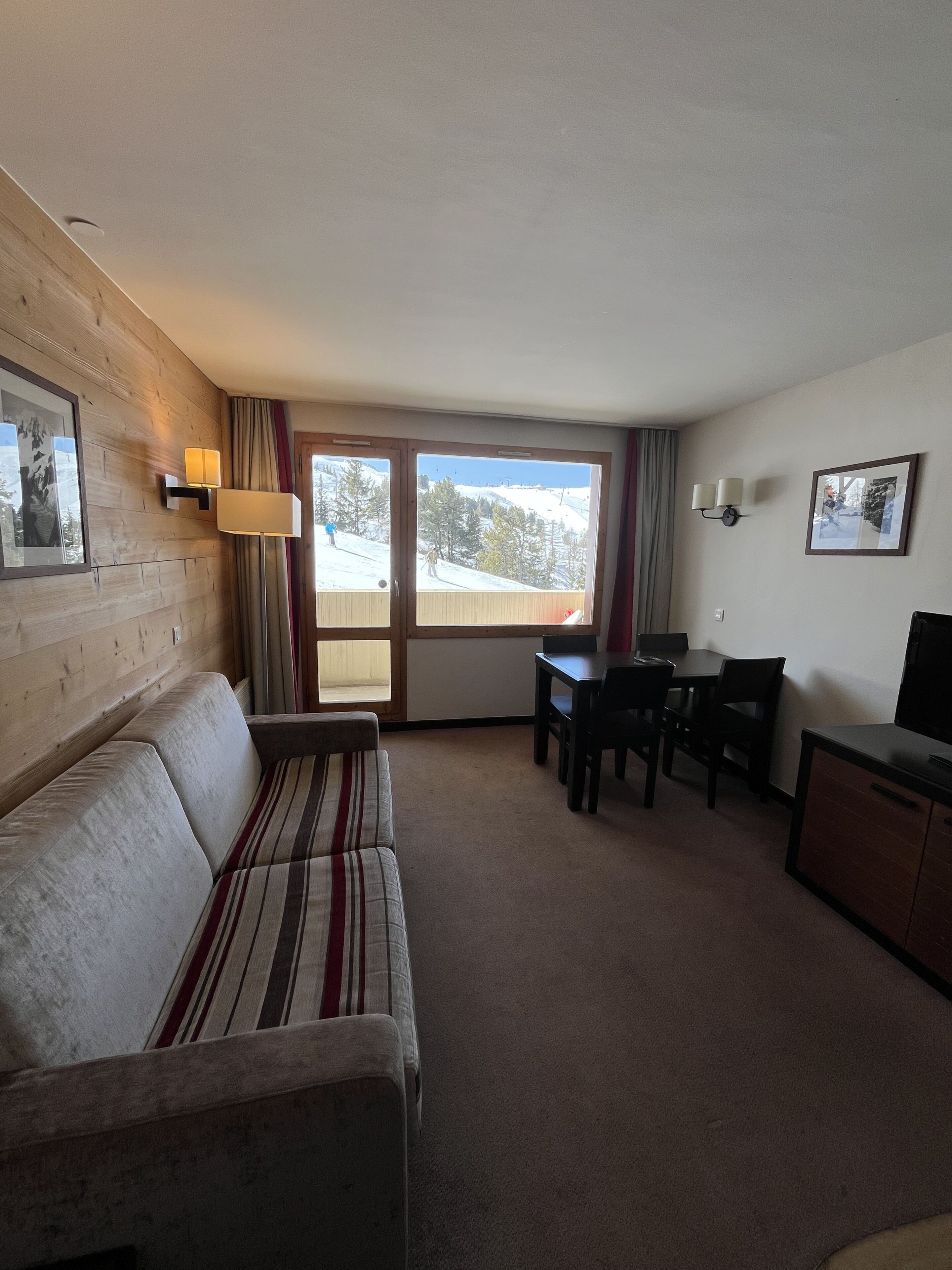 A room with a sofa, a dining table with chairs, a TV, and a window with a view of a snowy landscape.
