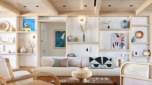 A modern living room with a sofa, two wooden chairs, a coffee table, and shelves with decorative items.