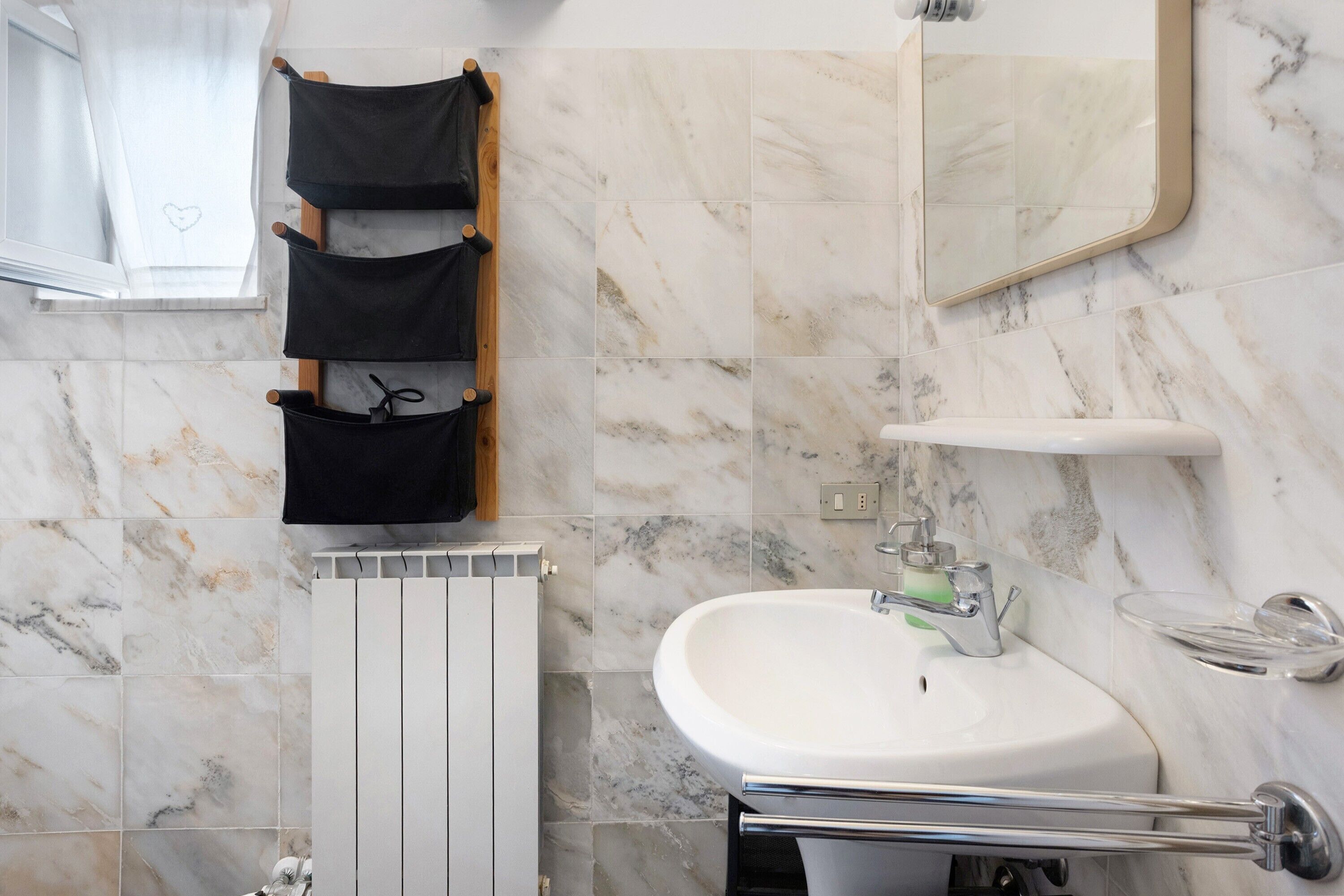 Een badkamer met een witte wastafel, spiegel, handdoekrek en radiator.