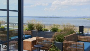 A terrace with wicker furniture and a view of a city skyline across a body of water.