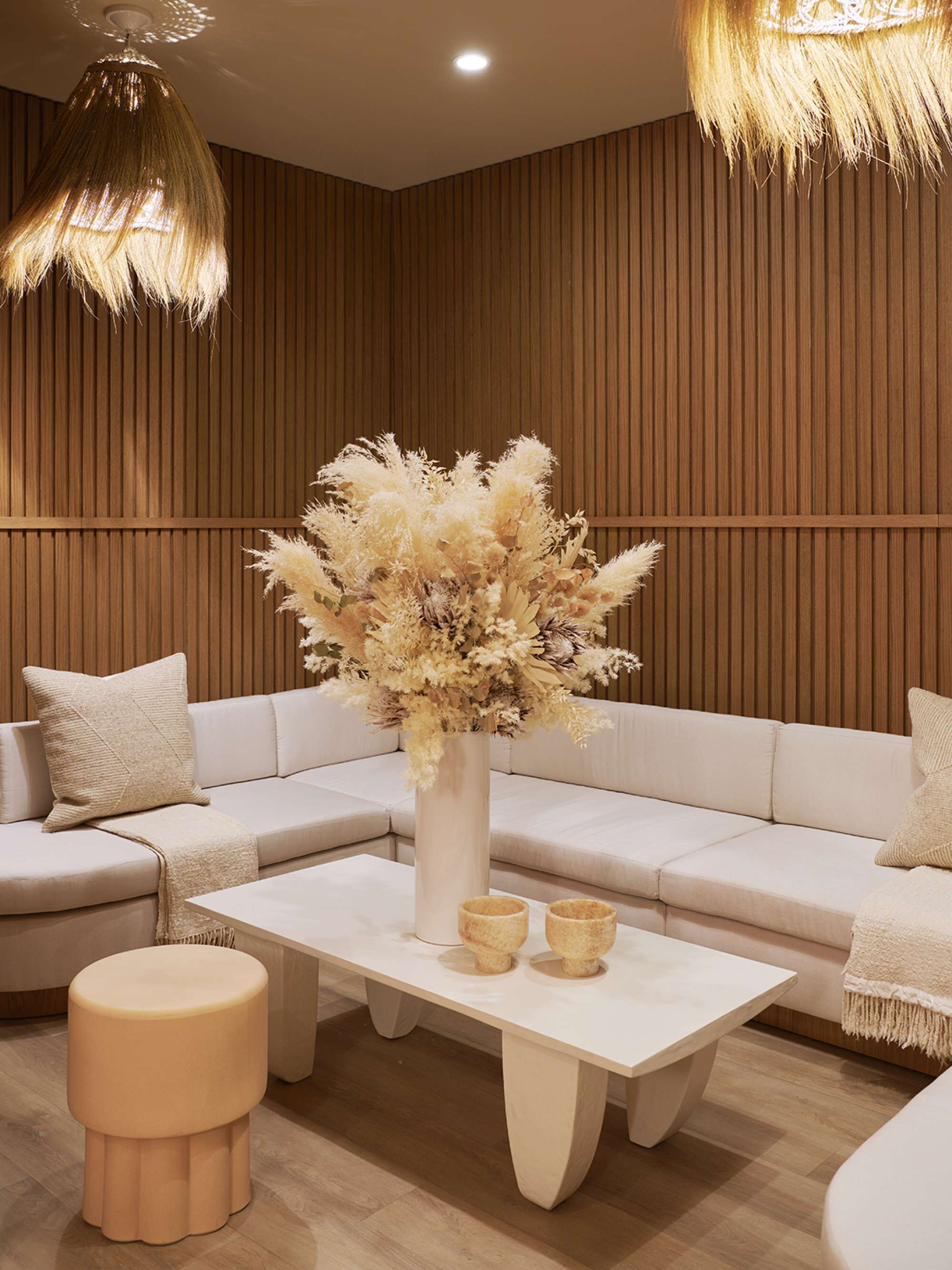 Ein modernes Wohnzimmer mit einer Eckcouch, einem runden Hocker, einem weißen Couchtisch und einer Vase mit Trockenblumen.