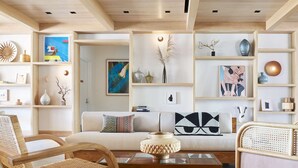 Un salon moderne comprenant un canapé, deux fauteuils en bois, une table basse et des étagères ornées d’objets décoratifs.