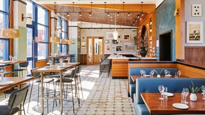 Ein Restaurant mit Holztischen und blauen Sitzbänken, großen Fenstern und einer gemusterten Decke.