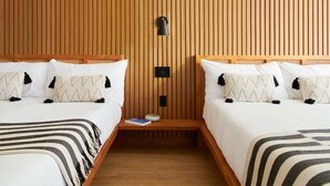 A hotel room with two beds, wooden paneling, a bedside table with a book, and a wall-mounted lamp.