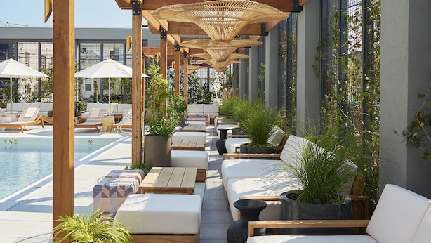 Un espace aménagé au bord de la piscine, avec des pergolas en bois, des chaises longues et des plantes en pot.